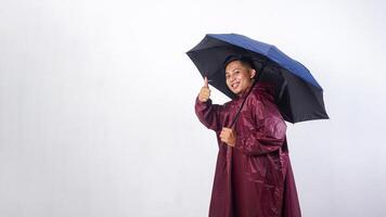 Happy Asian man in red raincoat holds umbrella and showing his thumb up isolated on white background photo