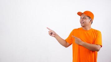 Asian deliveryman in orange t-shirt uniform poses as if he is pointing something in empty space area isolated on white background photo