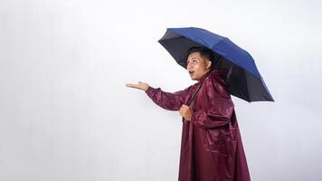 Worried Asian man in red raincoat and holds umbrella checking if rain stopped while looking up to the sky isolated on white background photo