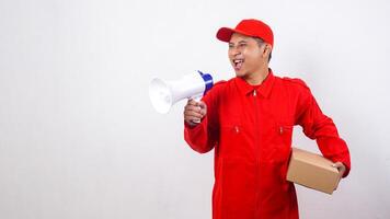 Asian Delivery man in red uniform carrying a package box parcel while shout using megaphone isolated on white background photo