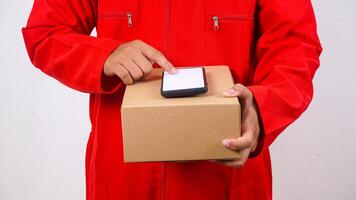 Delivery man in red uniform holding package box parcel with phone on top isolated on white background photo