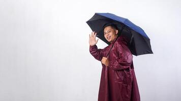 Happy Asian man in red raincoat and holds umbrella showing gesture to greeting people isolated on white background photo