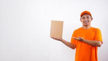 Asian deliveryman in orange t-shirt uniform poses as if he is presenting a package box parcel isolated on white background photo