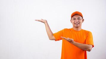 Asian deliveryman in orange t-shirt uniform poses as if he is presenting something in empty space area isolated on white background photo