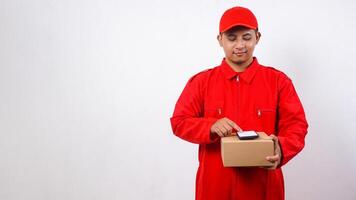 Asian Delivery man in red uniform holding package box parcel with phone on top isolated on white background photo
