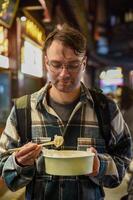 Russian tourist holding a crab and pork dumpling with chopsticks, looking at it before eating, on Yuyuan Old Street in Shanghai, wearing a plaid shirt photo
