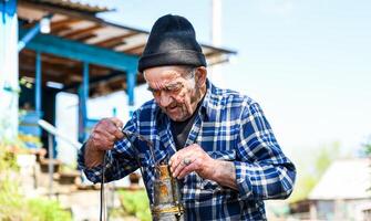 Elderly Russian man in a rural village holding a drainage pump with both hands, checking equipment under the open sky simple village routine in retirement photo