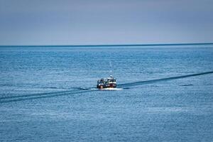 Fishing Boat in Ocean with Wake at Seahouses Harbour, UK photo