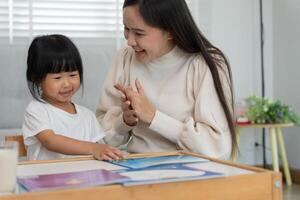 Happy Asian mother relax and read book with baby time together at home. parent sit on sofa with daughter and reading a story. learn development, childcare, laughing, education, storytelling, practice photo