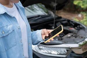 broken car repair. Woman uses mobile phone check insurance premiums through application due to car accident . Find garage to get car fixed during country tour, waiting for help, emergency. photo