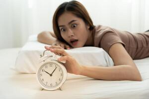 Shocked Asia woman looking at clock alarm, lady is late appointment or work or class study, overslept, difficulty get up in mornings, time worried, not on time, sleepy, over due, Hurry up time photo
