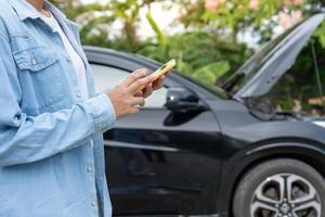 broken car. repair. Woman uses mobile phone check insurance premiums through application due to car accident . Find garage to get car fixed during country tour, waiting for help, emergency. photo