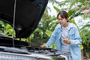 Woman uses mobile phone check insurance premiums through application due to car accident . Find garage to get car fixed during country tour, waiting for help photo