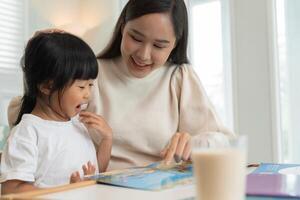 Happy mother relax and read book with baby time together at home. parent sit on sofa with daughter and reading a story. learn development, childcare, laughing, education, storytelling, practice. photo