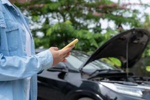 breakdown, broken car. Woman uses mobile phone check insurance premiums through application due to car accident . Find garage to get car fixed during country tour, waiting for help, emergency. photo