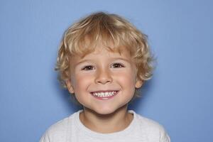 Happy smiling boy with blonde curly hair on blue background. photo