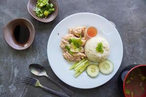 Hainanese chicken rice or nasi hainan or rice steamed with chicken soup served with cucumber slice, broth, and sauce, photo