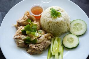 Hainanese chicken rice steamed with chicken soup served with cucumber slice, broth, and sauce photo