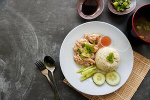 Hainanese chicken rice or nasi hainan or rice steamed with chicken soup served with cucumber slice, broth, and sauce. photo