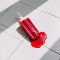 A red popsicle on a tile floor photo