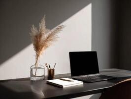 A laptop sitting on a desk with a vase of pampas grass photo