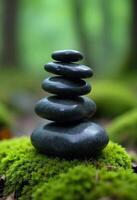 Stack of smooth black stones on top of a vibrant green moss, blurred background with trees, zen concept photo