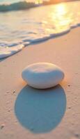 A white stone on the sand, the sea in the background, golden hour photo