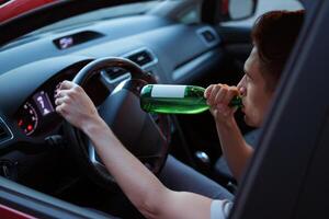 Driver consumes alcohol while operating vehicle in a parked car at dusk photo