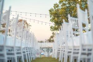 Elegant wedding long table with candle, white rose flower and white chairs in the garden photo