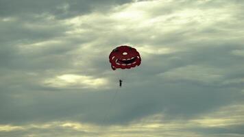 Tourists fly on a red parachute on a rope against the backdrop of a sunset video