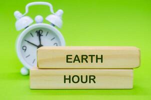 Wooden blocks with Earth Hour text placed on green surface with alarm clock background. photo
