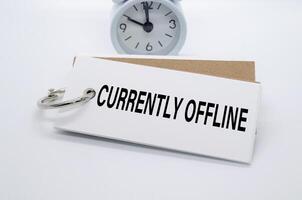 Currently Offline text on white notepad with alarm clock on white background. Away from office concept. photo