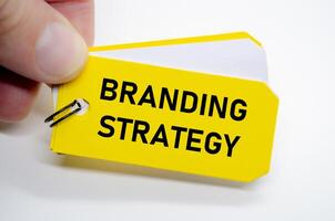 Branding strategy in bold black font on yellow sticky note with hand holding the concept. photo