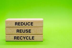 Wooden blocks with Reduce, Reuse and Recycle text placed on green surface. Symbolizing commitment to eco friendly habits and waste reduction. photo