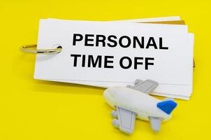 Personal Time Off text on white notepad with toy airplane on yellow cover background. Away from office concept photo