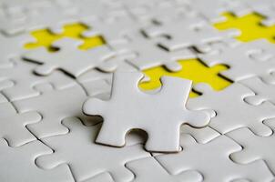 Close up of white jigsaw puzzle pieces placed on a bright yellow background with customizable space on jigsaw for text or ideas. photo