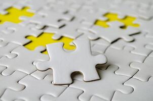 Side close up of white jigsaw puzzle pieces placed on a bright yellow background with customizable space on jigsaw for text or ideas. photo