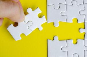Hand matching white puzzle pieces lying on a vibrant yellow surface highlighting contrast and precise alignment photo