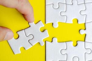 Top view of hand taking out of connecting white jigsaw puzzles into its original position. Solution or teamwork concept photo