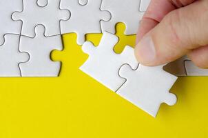 Side view of hand holding jigsaw puzzle pieces on a bright yellow background with customizable space on jigsaw for text or ideas photo