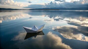 Paper boat floats on calm water reflecting clouds during sunset photo