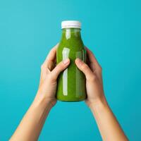 Hands presenting a bottle of vibrant green smoothie against a cyan backdrop photo