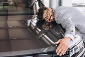 Smiling man hugging a car in a modern showroom photo