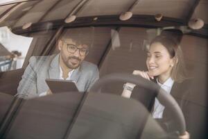 Car salesman showing tablet to customer sitting in new car photo