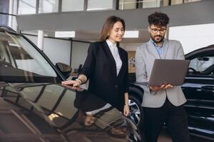 Car salesman showing features on laptop to customer buying new car photo