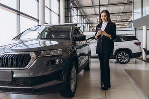 Saleswoman using smartphone near new car in showroom dealership photo