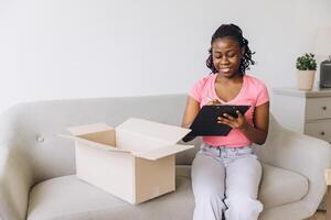 Young african american woman checking delivery list and preparing cardboard box for shipping photo