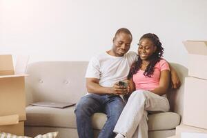 Happy African American Couple Using Smartphone While Relaxing on Sofa After Moving into New Home photo