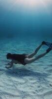 Woman glides underwater over sandy sea bottom in blue ocean with sunshine, freediving with sexy woman video