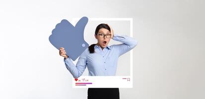 A surprised influencer stands in a studio, holding a large like symbol and expressing excitement. The backdrop features a collage of social media elements, enhancing the theme of digital content. photo